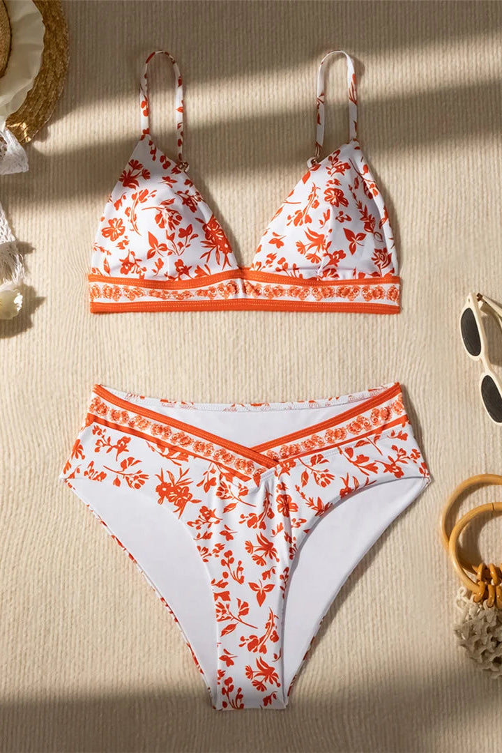 White bikini with orange floral pattern on a beige surface with accessories.
