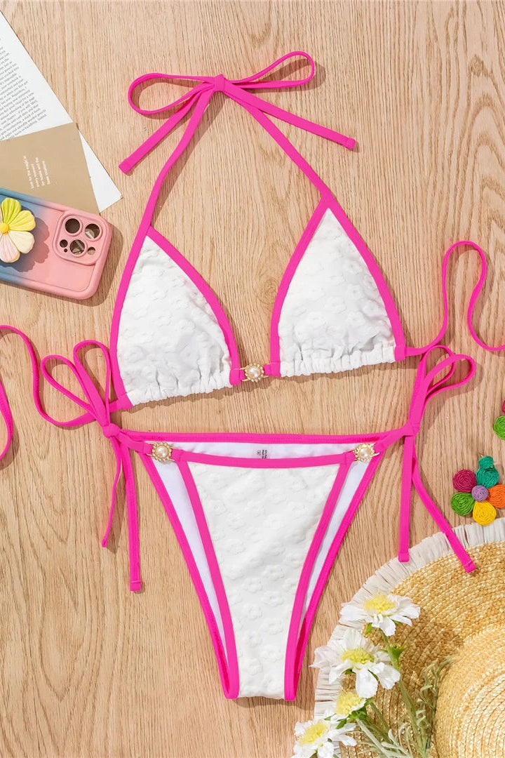 White bikini with pink straps on a wooden surface with accessories.