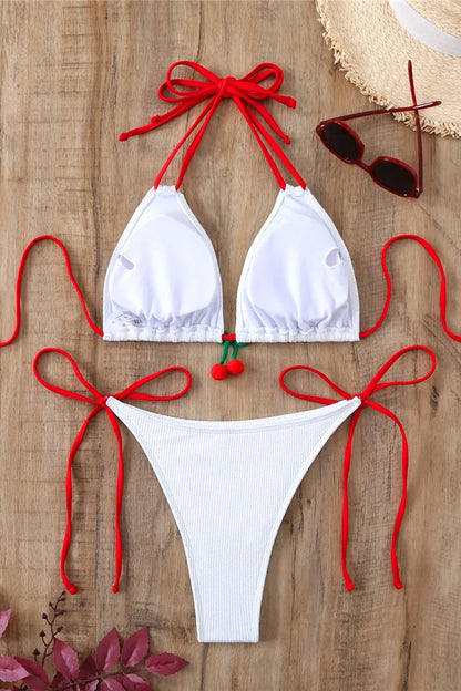 White bikini with red straps on a wooden surface, accompanied by sunglasses and a hat.