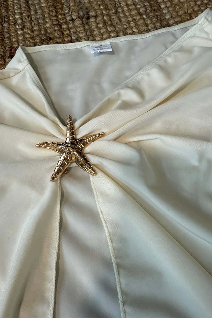 White skirt with a starfish brooch on a textured surface