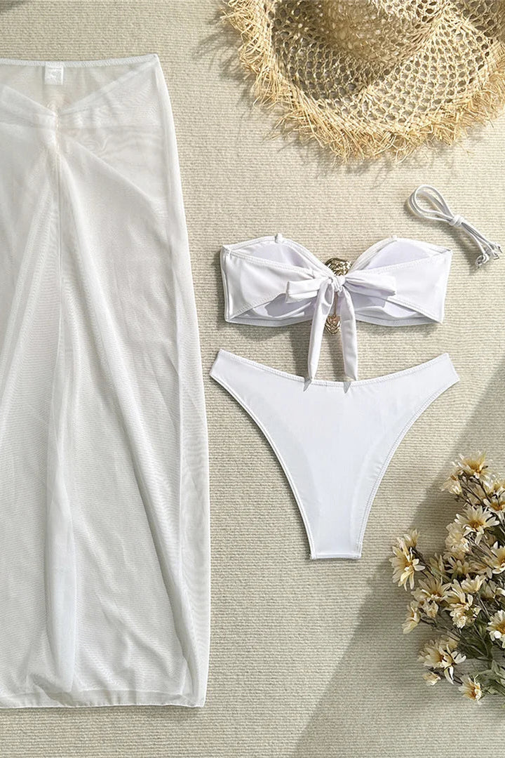White swimsuit with matching cover-up on a textured surface with a hat and flowers.