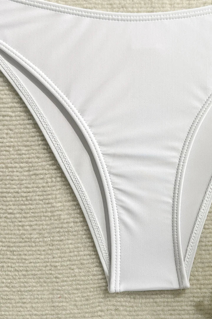 White thong on a beige fabric background with a small flower arrangement.