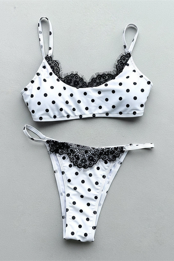 White two-piece bikini set with black polka dots and black lace trim, laid flat on a light gray background.
