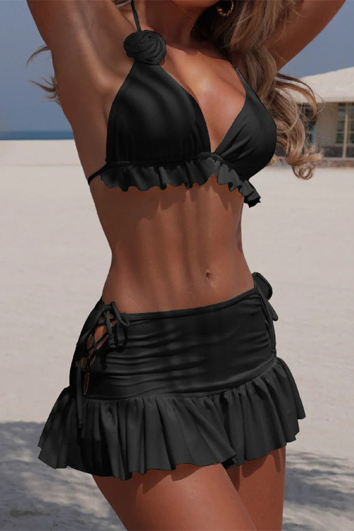 Woman in a black bikini with ruffled details on a beach.