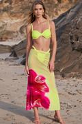 Woman in a bright yellow bikini top and floral skirt on a beach.