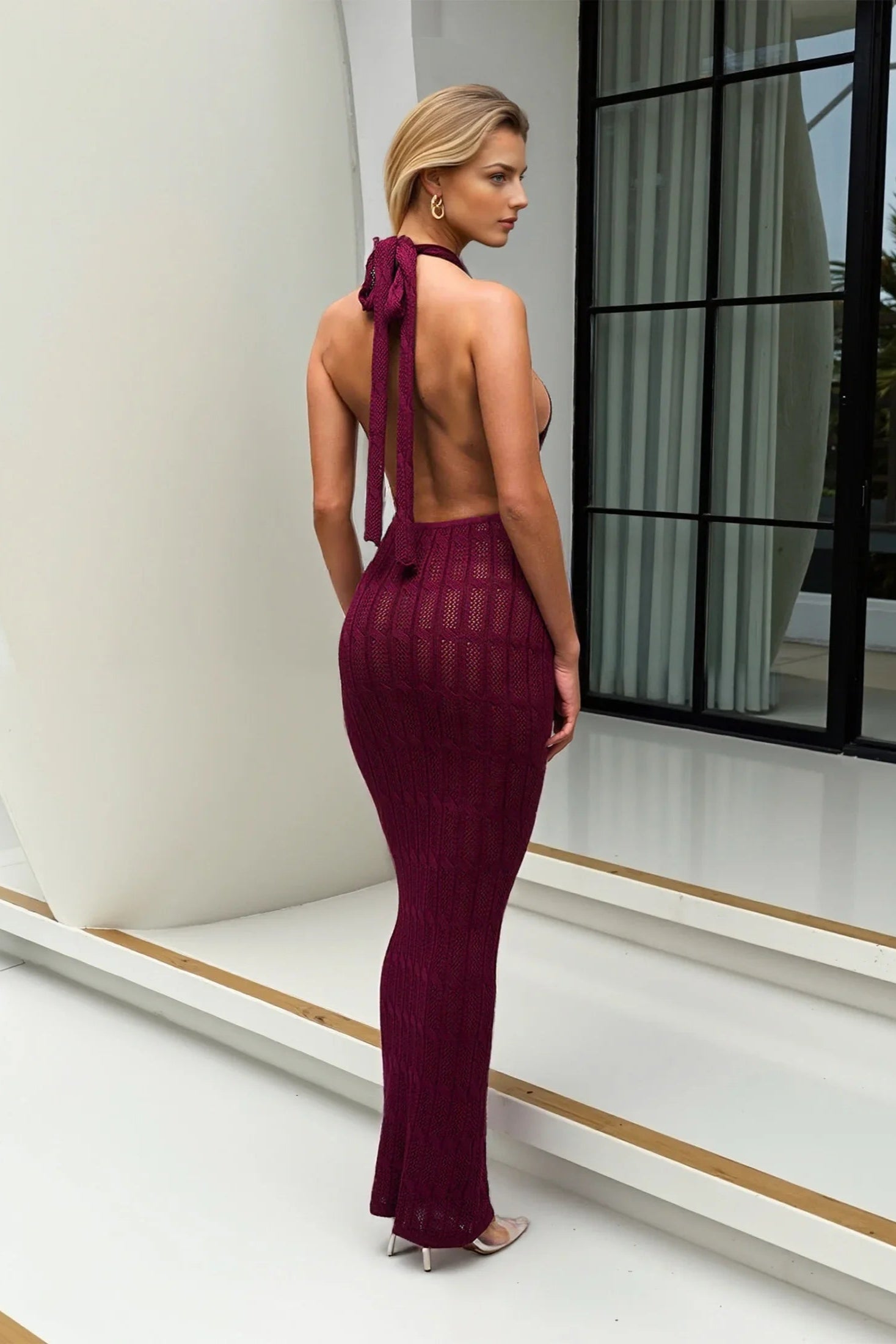 Woman in a burgundy cover up beach wear standing in a modern indoor setting.