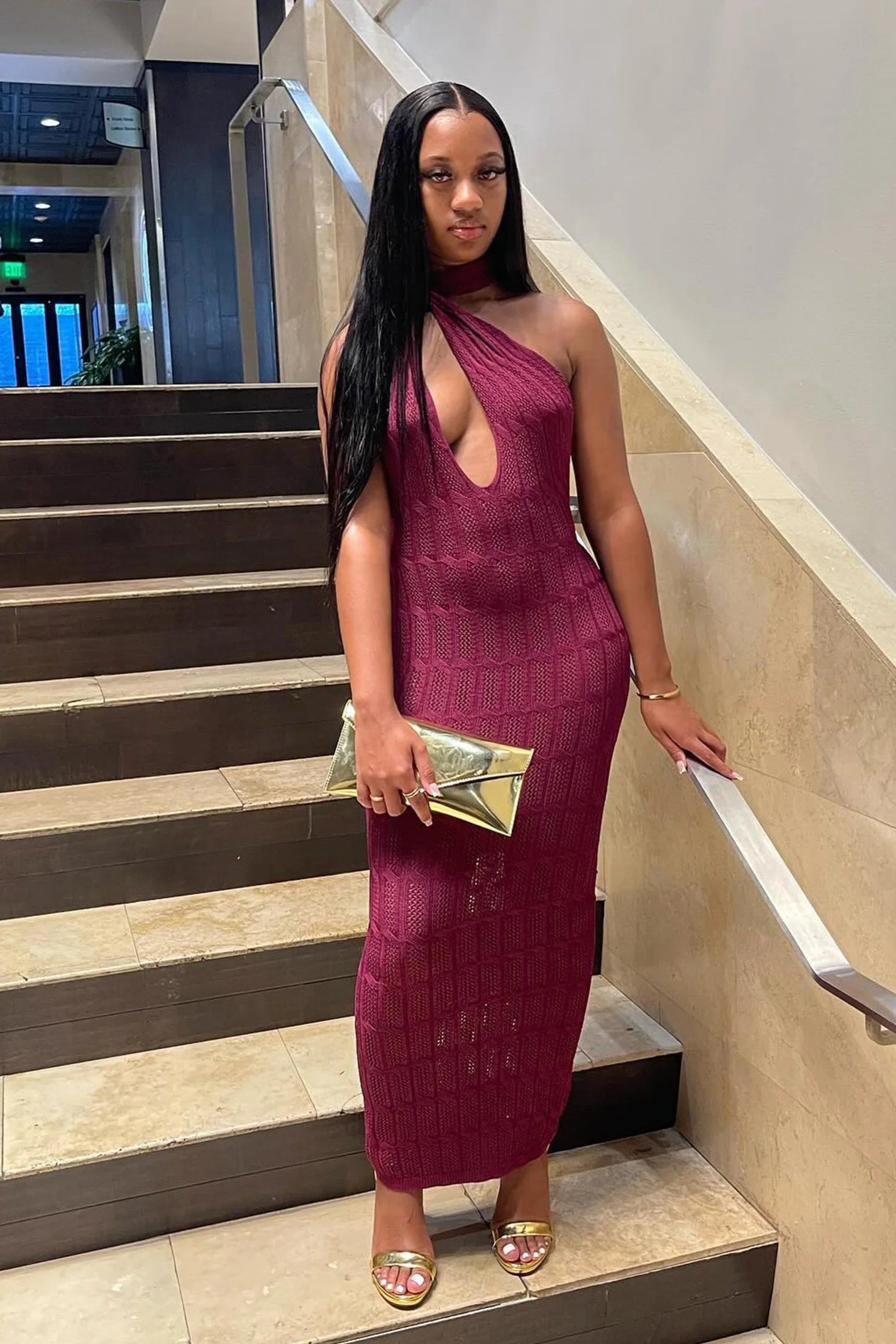 Woman in a burgundy dress standing on a staircase indoors