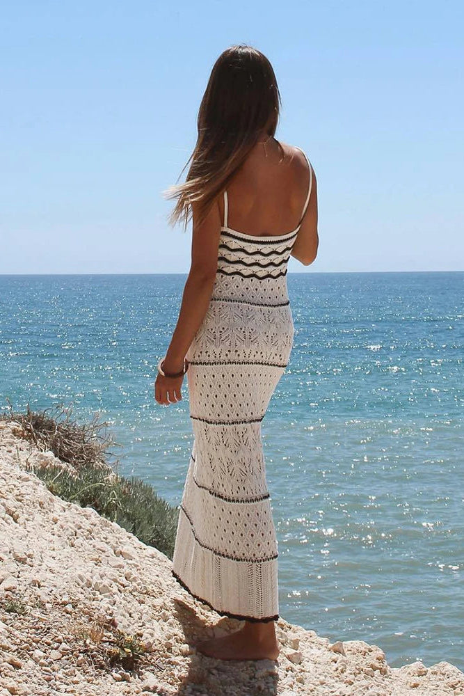 Woman in a crochet dress standing on a cliff overlooking the ocean.