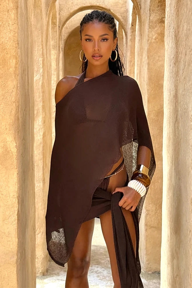 Woman in a dark brown cover top and skirt standing in a sunlit archway with beige stone walls.