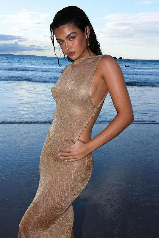 Woman in a gold cover up  dress standing on a beach with ocean waves in the background