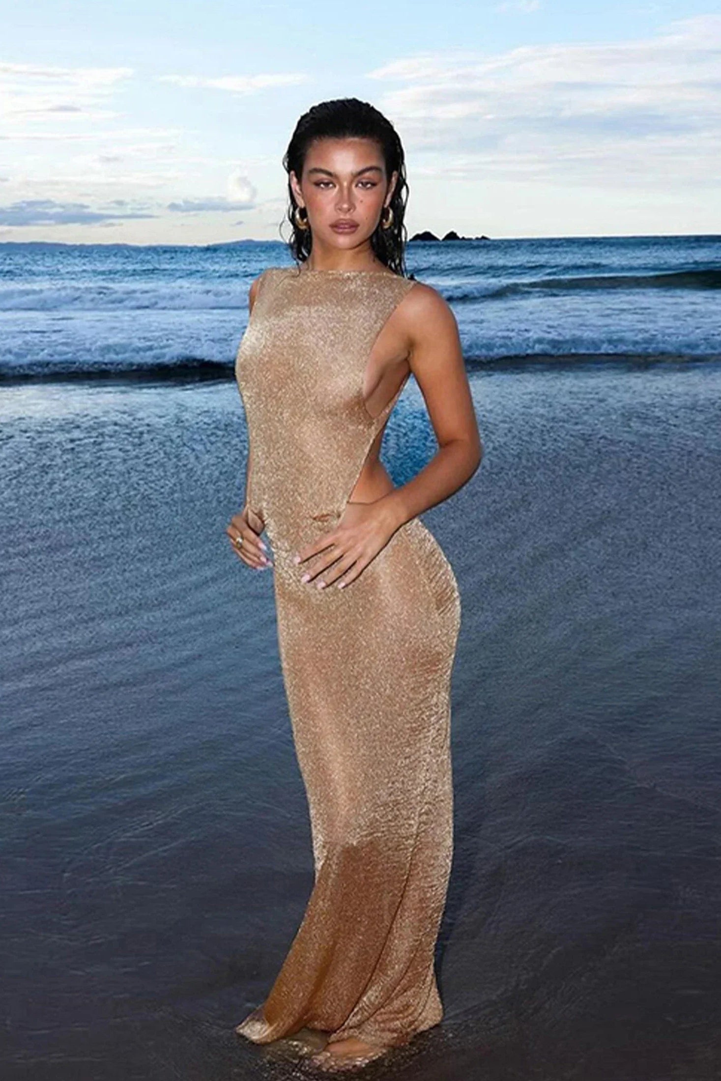 Woman in a gold dress standing on a beach with ocean waves in the background