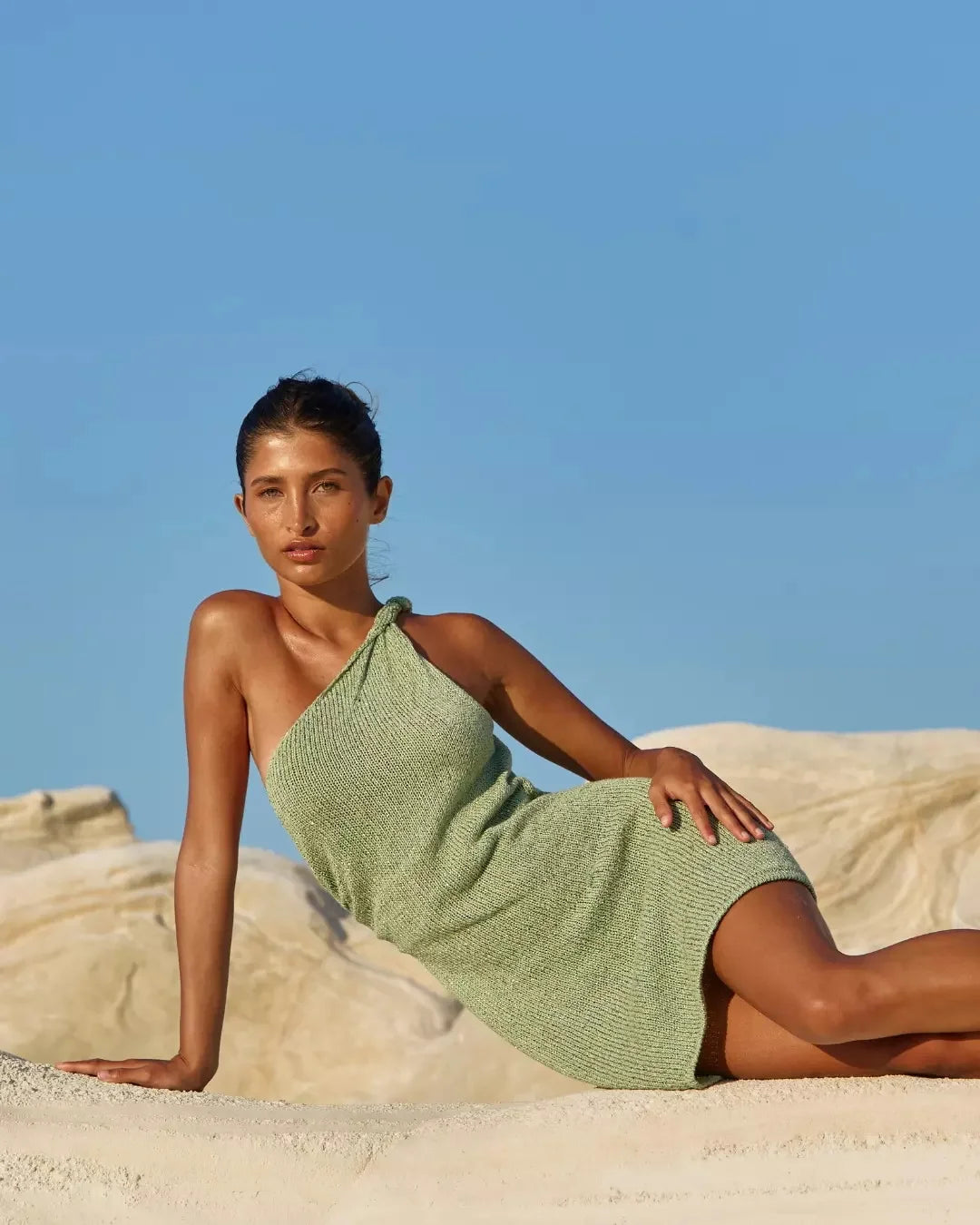 Woman in a green dress sitting on sand with a clear blue sky