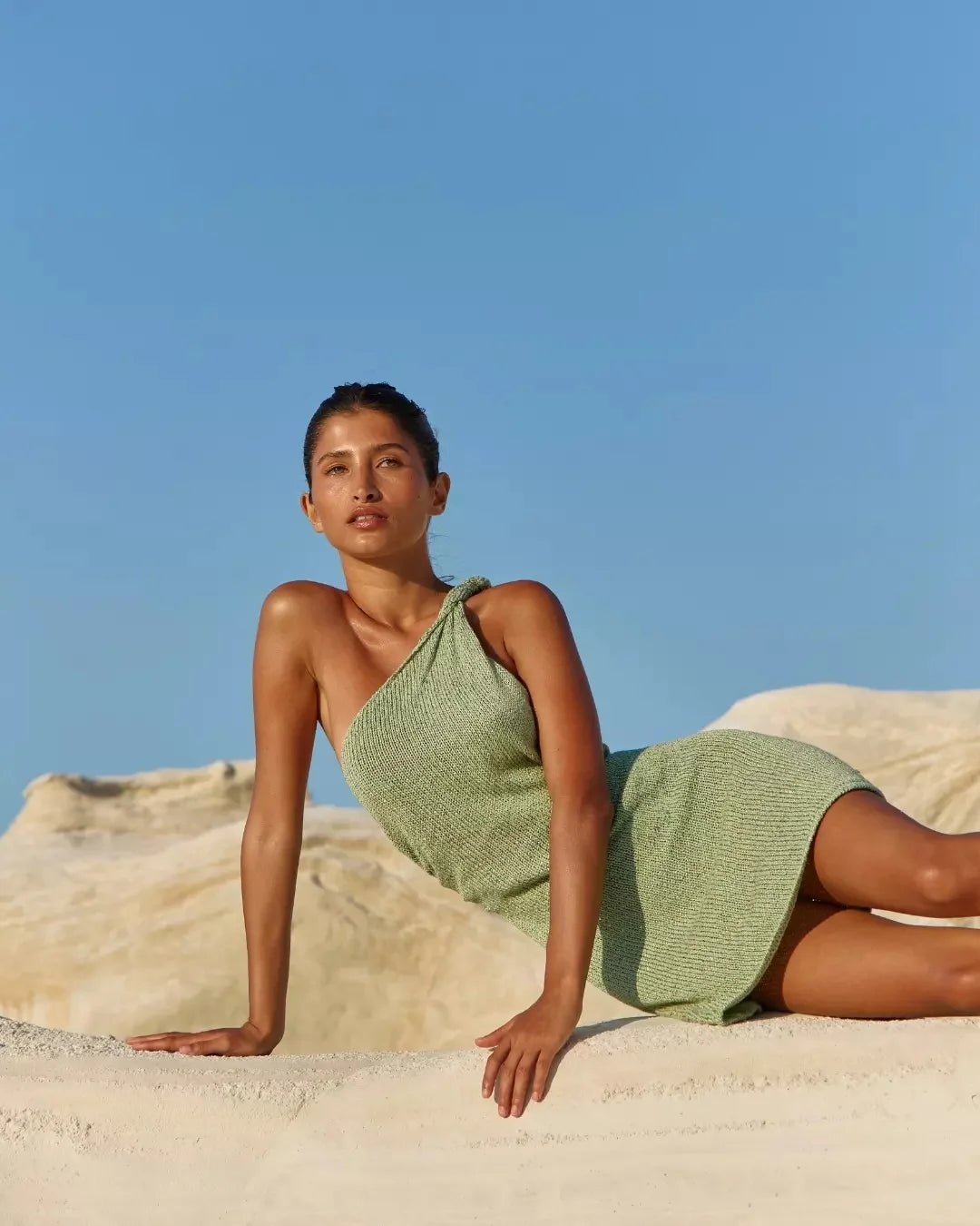 Woman in a green dress sitting on sand with a clear blue sky dcostaa beach wear for womens