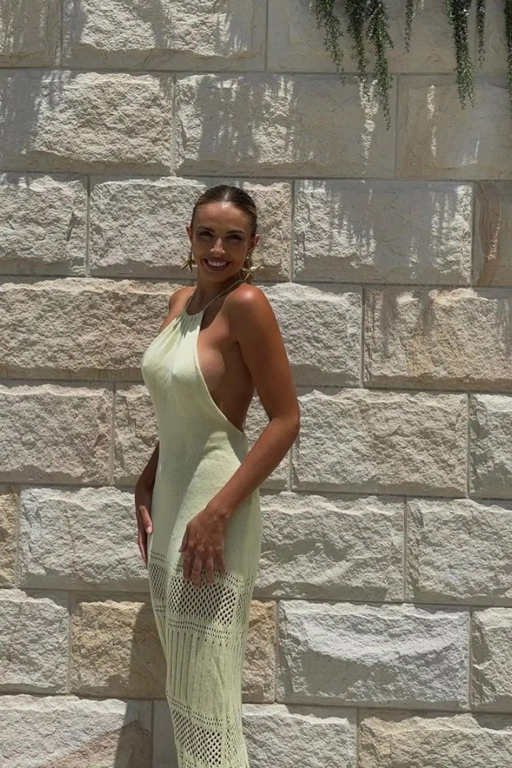 Woman in a light cream dress standing against a stone wall.