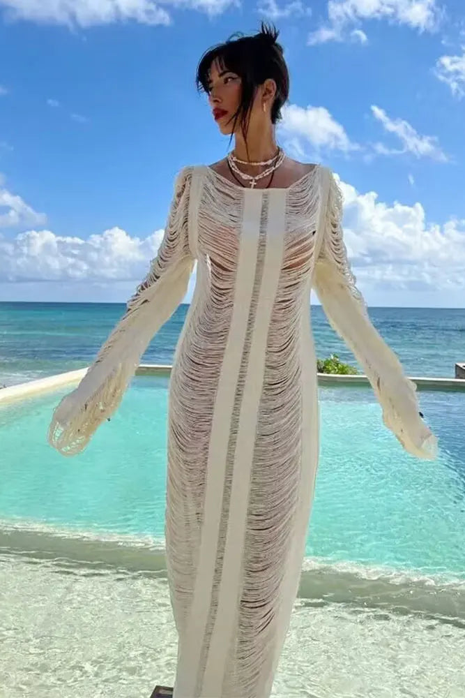 Woman in a long, light-colored dress standing by a pool with ocean view