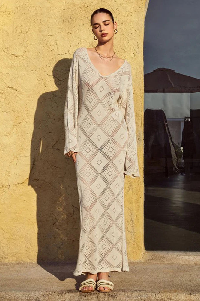 Woman in a patterned dress standing against a textured wall with a dark umbrella in the background.