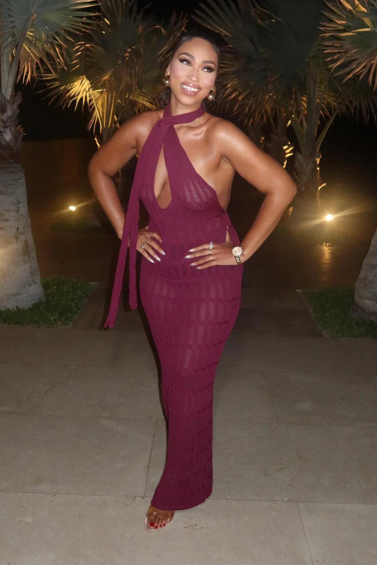 Woman in a purple cover up dress posing outdoors with palm trees in the background