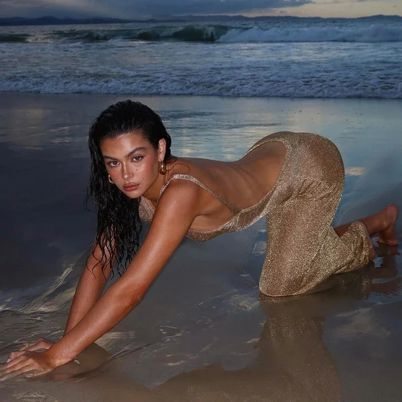 Woman in a sparkly dress kneeling on a beach with waves in the background