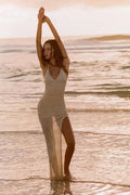 Woman in a swimsuit cover up standing in shallow water at the beach