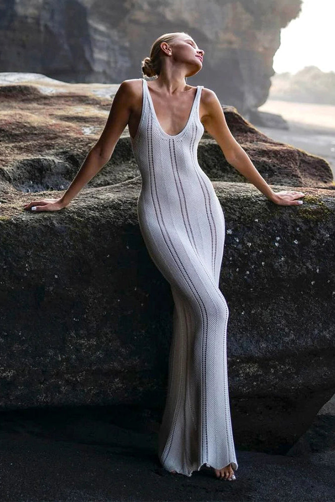 Woman in a white cover up dress sitting on a rocky cliff with a scenic background