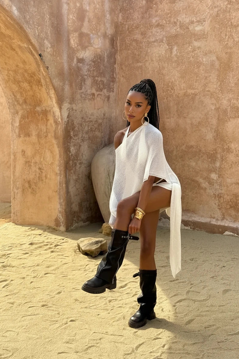 Woman in a white cover up half shoulder top and sarong sitting against a textured wall.