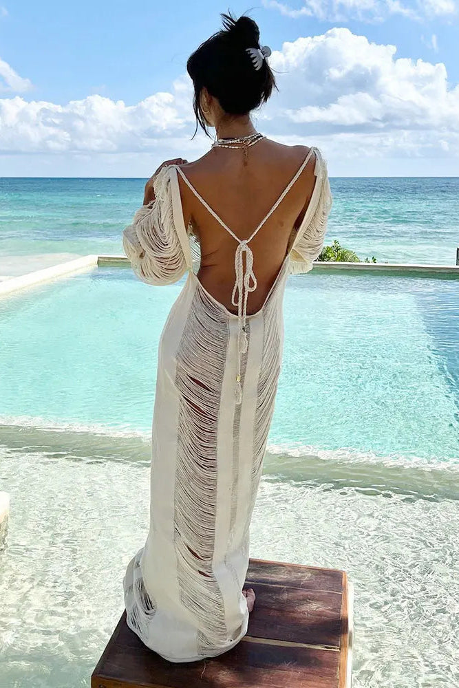 Woman in a white cover up with a open back standing by a pool with ocean view