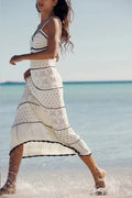Woman in a white crochet beach dress walking on a beach.