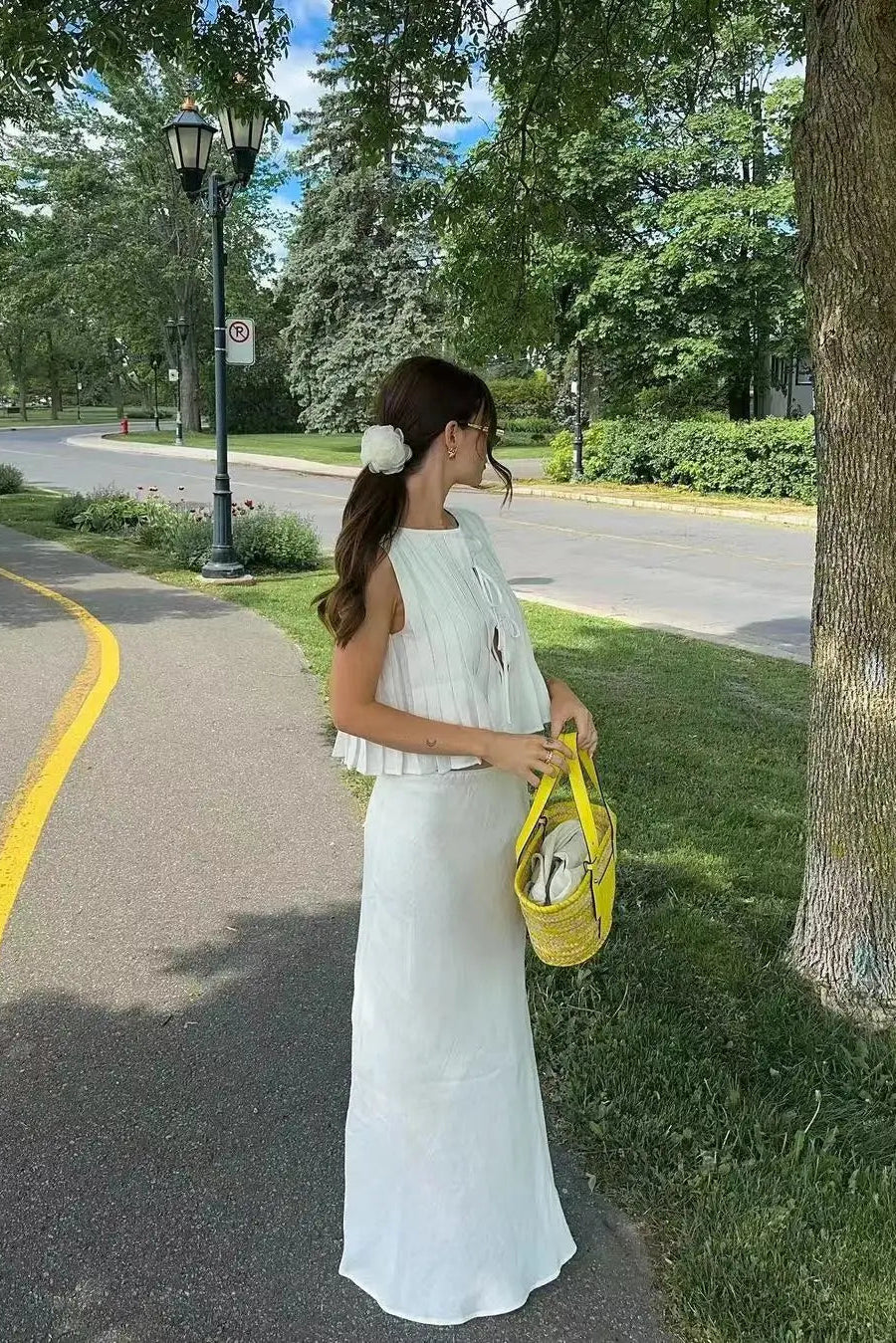 Woman in a white dress holding a yellow bag on a tree-lined street.