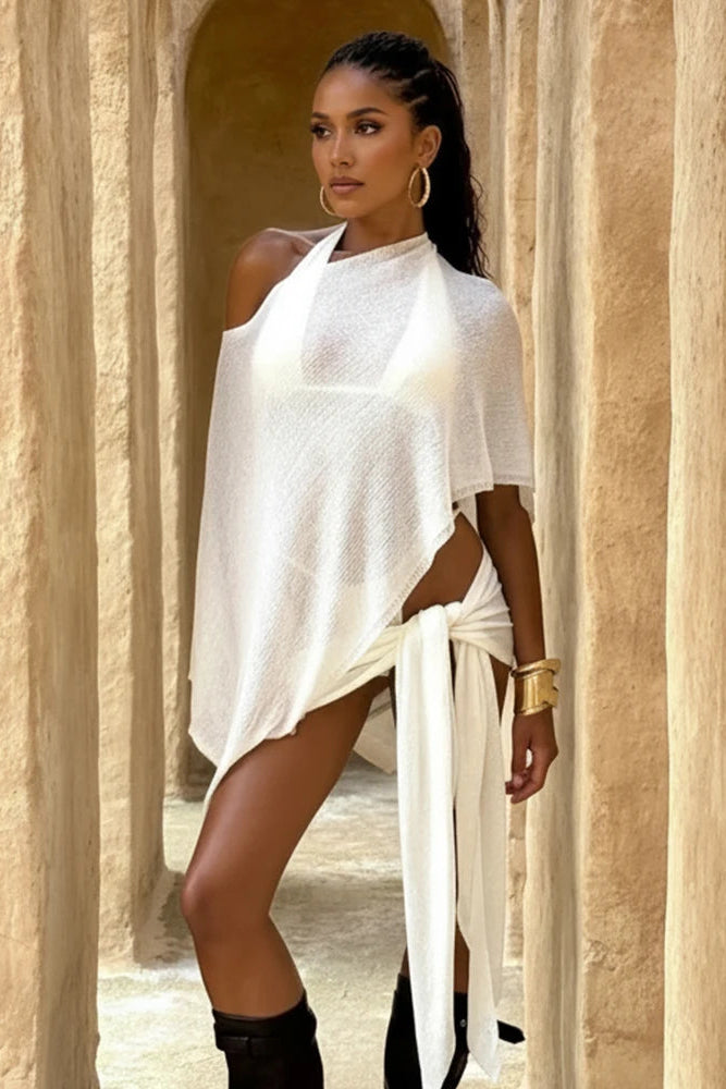 Woman in a white dress standing in a sunlit archway with beige stone walls.