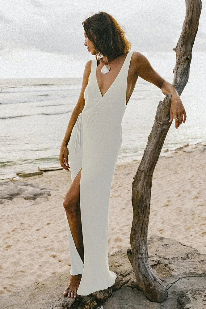 Woman in a white dress standing on a beach with a large piece of driftwood.
