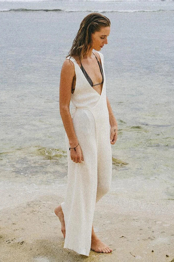 Woman in a white dress standing on a beach with water in the background
