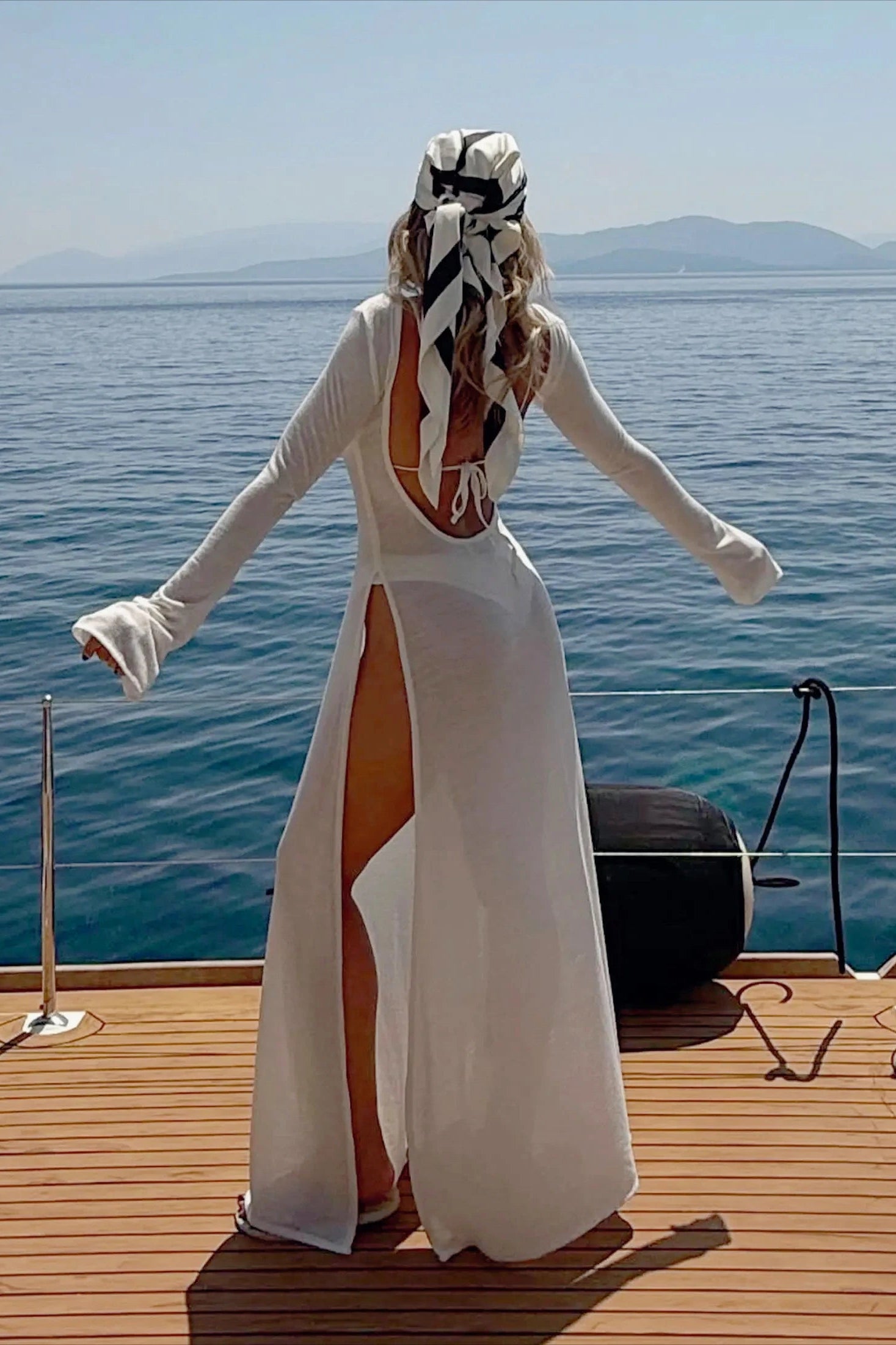 Woman in a white dress with a high slit standing on a boat deck with ocean view