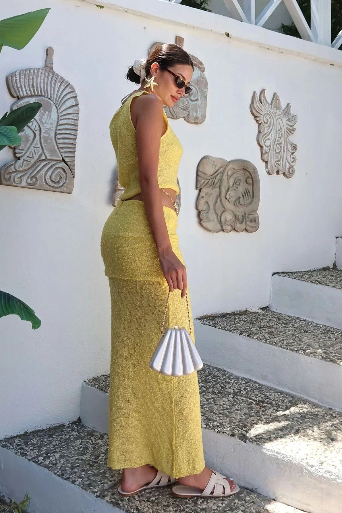 Woman in a yellow 2 piece set standing in front of a white wall with decorative elements.