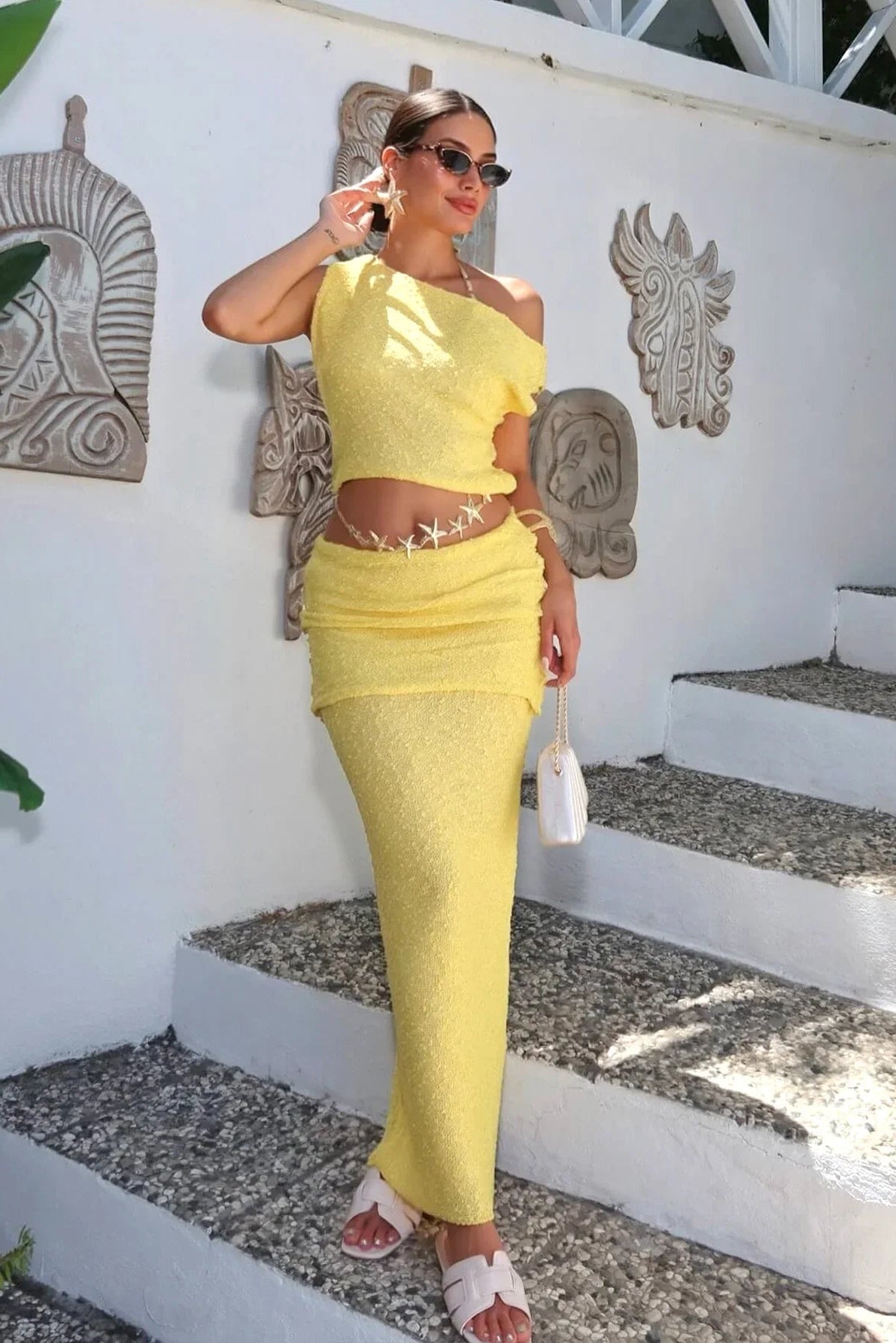 Woman in a yellow outfit standing on steps with decorative wall art in the background