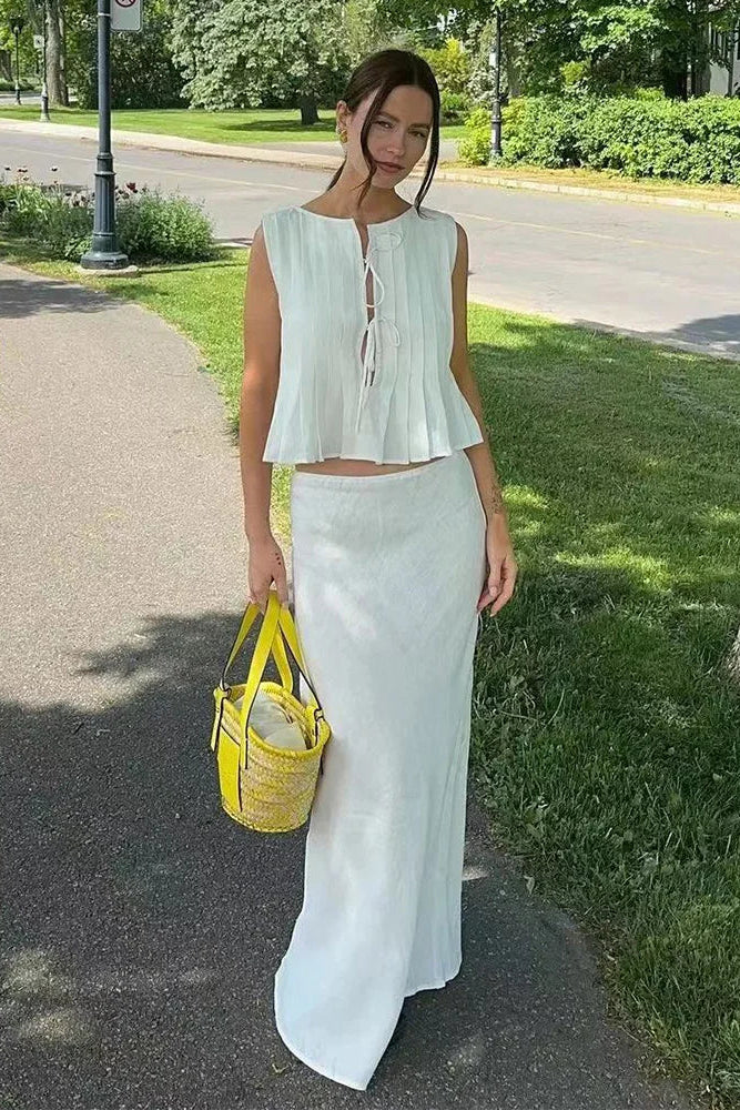 Woman in white top and white skirt holding a yellow bag on a sidewalk.