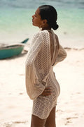 Woman wearing a beige crochet cover-up on a beach with a boat in the background