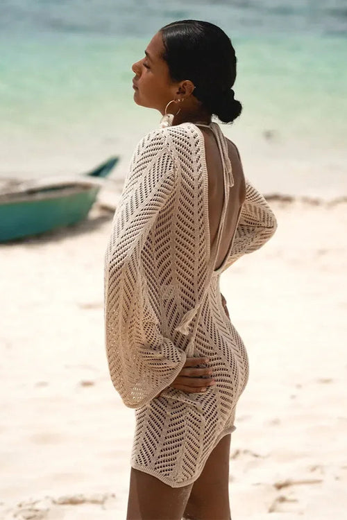 Woman wearing a beige crochet cover-up on a beach with a boat in the background