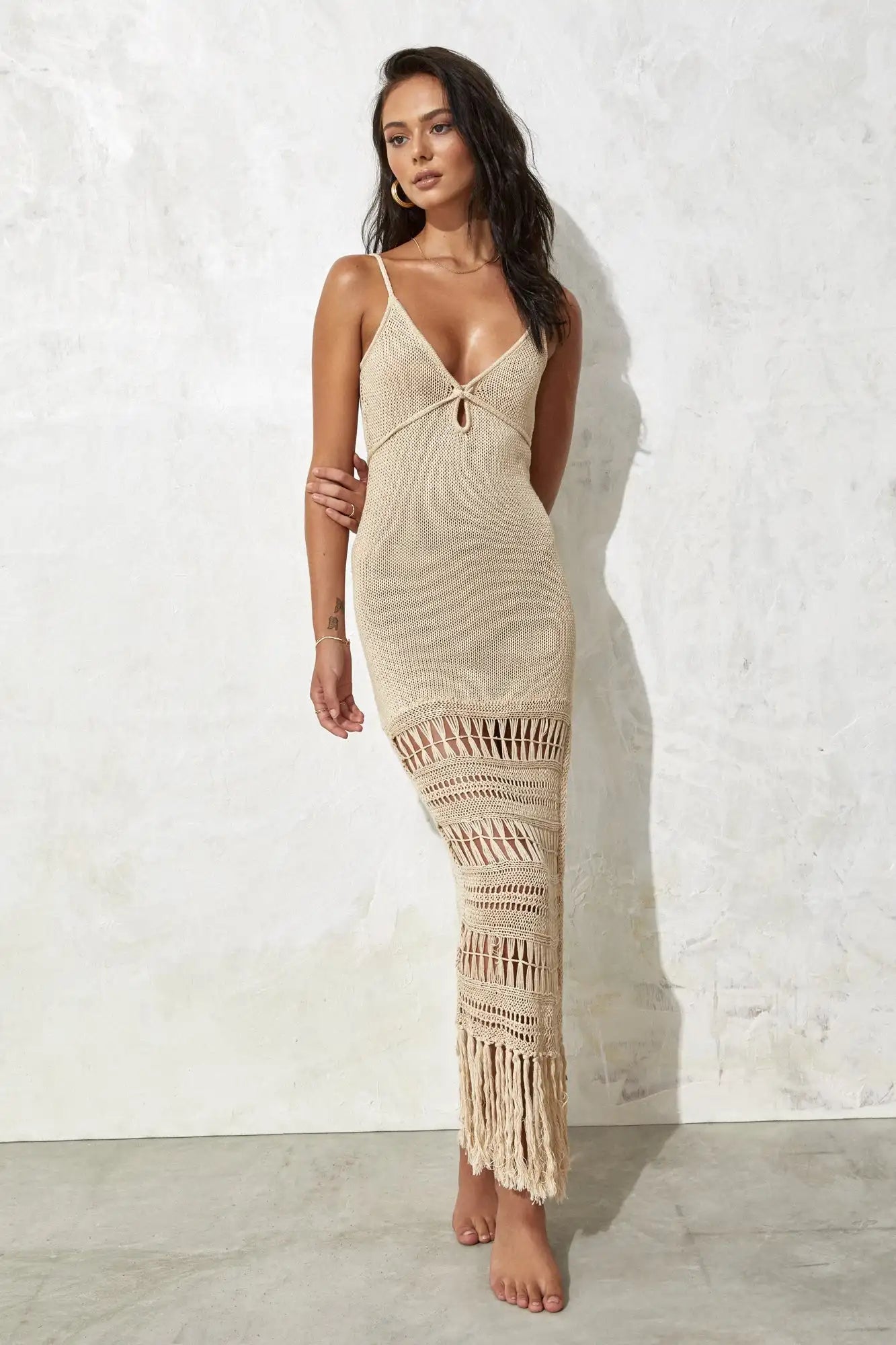 Woman wearing a beige dress with crochet details against a white wall.