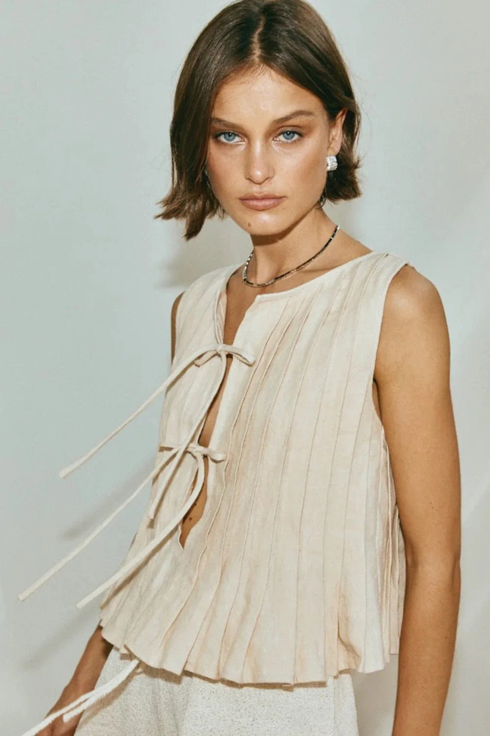 Woman wearing a beige sleeveless top with a plain background