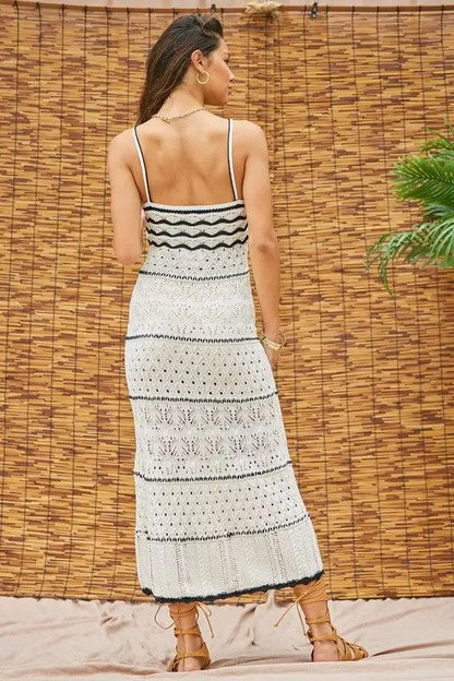 Woman wearing a black and white patterned vacation beach dress against a woven wall.