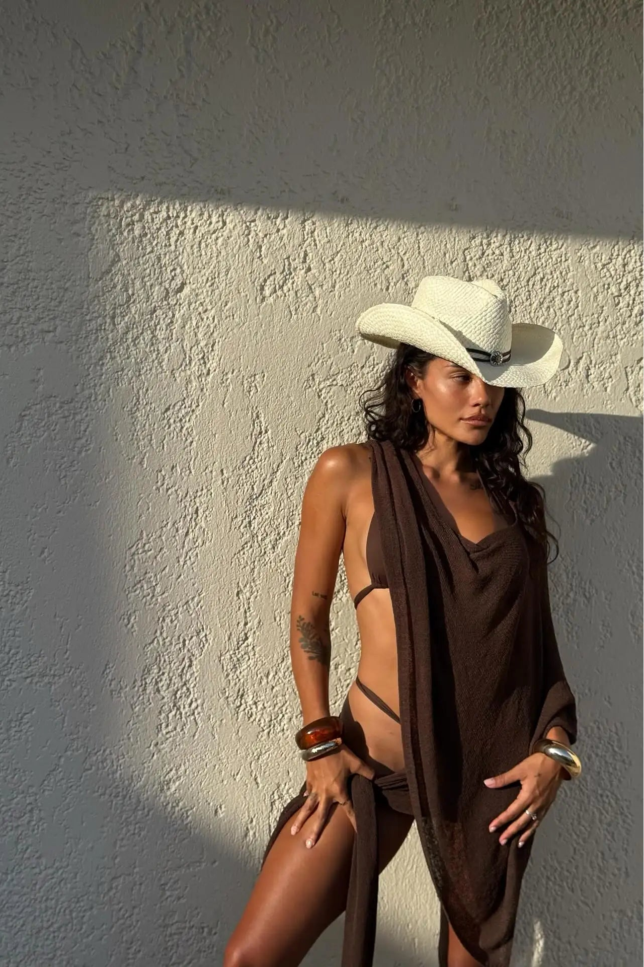 Woman wearing a cowboy hat and brown cover up set against a textured wall