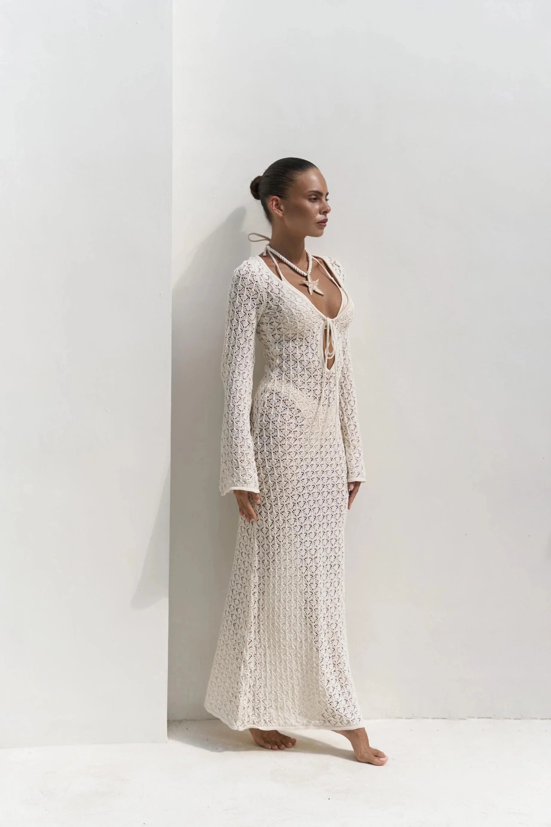 Woman wearing a long, light-colored textured see through dress against a white background
