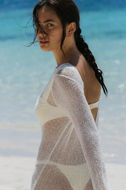 Woman wearing a sheer cover-up on a beach with clear blue water.