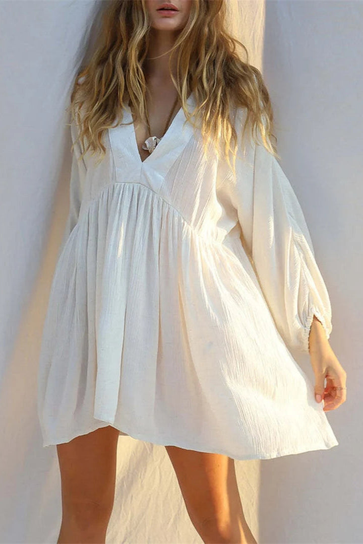 Woman wearing a white cover up dress against a plain background