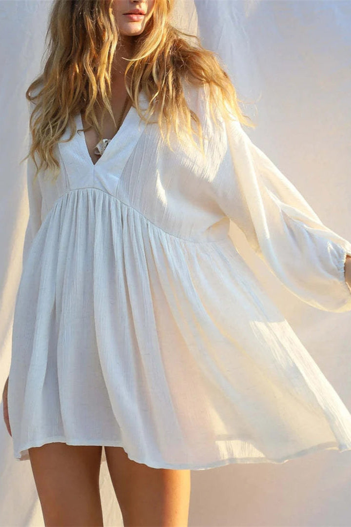 Woman wearing a white cover up dress with sheer sleeves against a light background