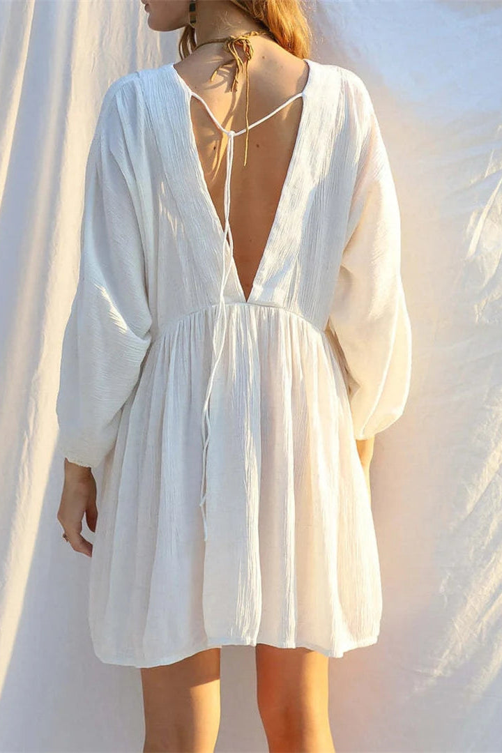 Woman wearing a white cover up tunic dress with a deep neckline against a soft, blurred background
