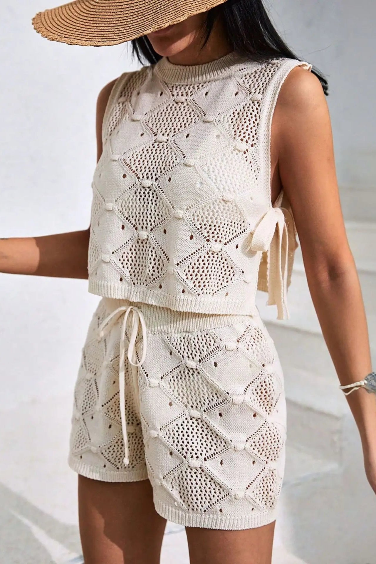 Woman wearing a white crochet outfit with a matching hat against a neutral background