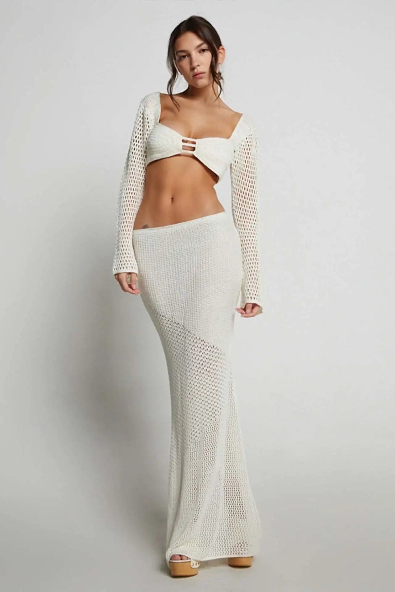 Woman wearing a white crochet two piece outfit on a plain background