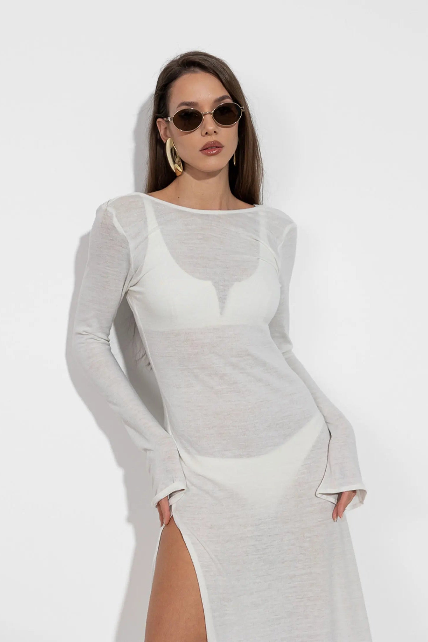 Woman wearing a white dress with long sleeves and a slit on a white background