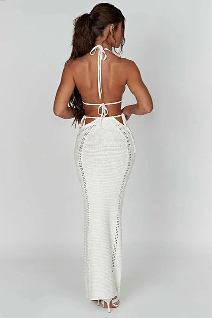 Woman wearing a white open-back bikini top and cover up skirt on a plain background